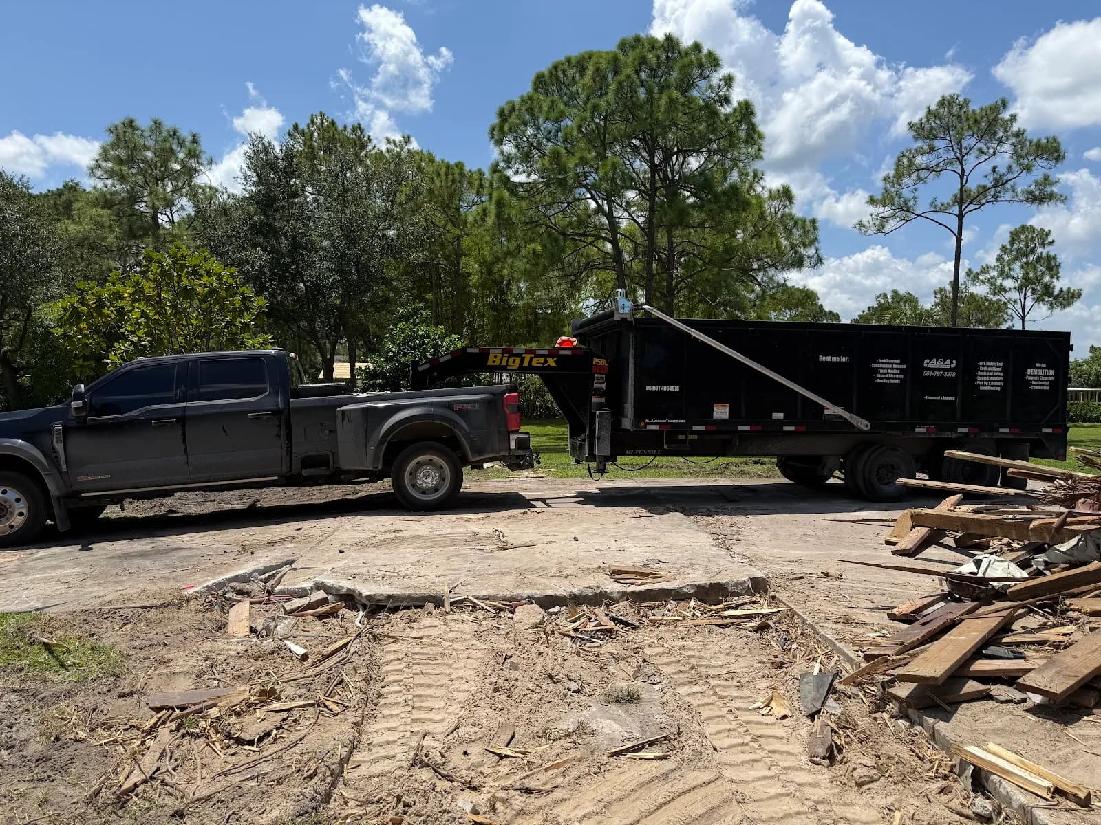Pickup towing a dump trailer at a demolition site with wood debris