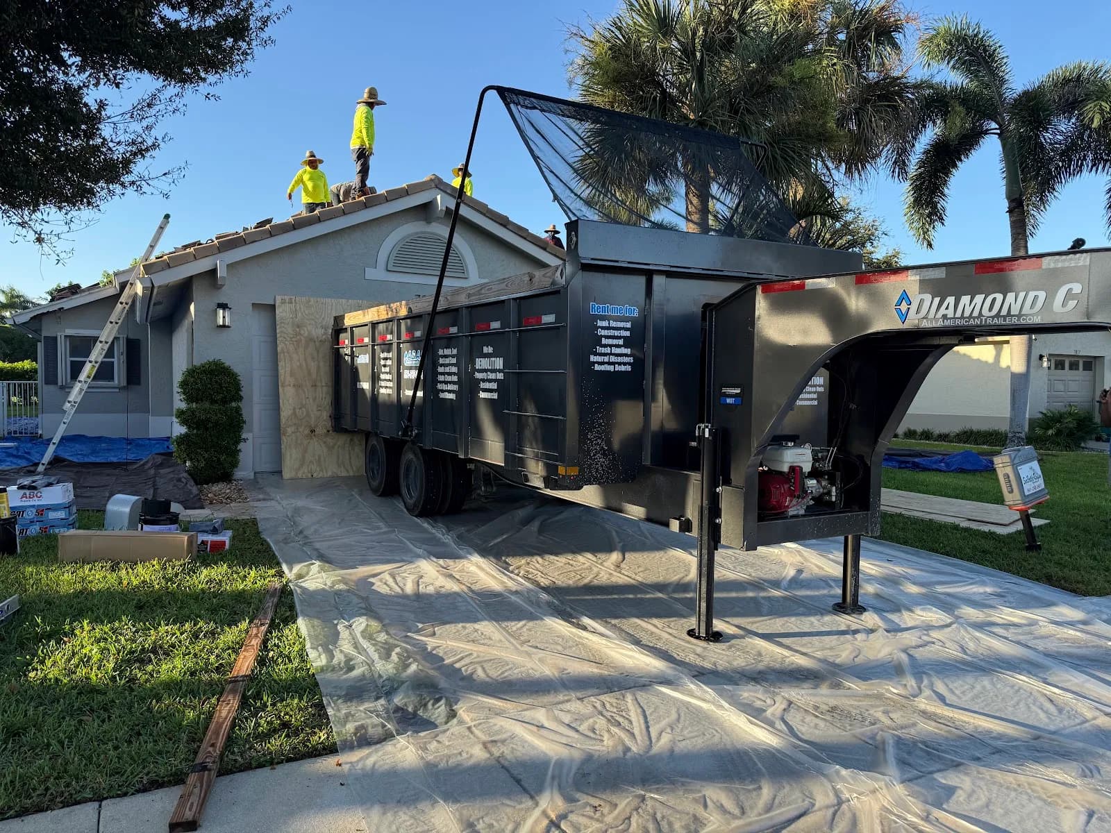 Dump trailer beside a house during a re-roof with roofers on the roof