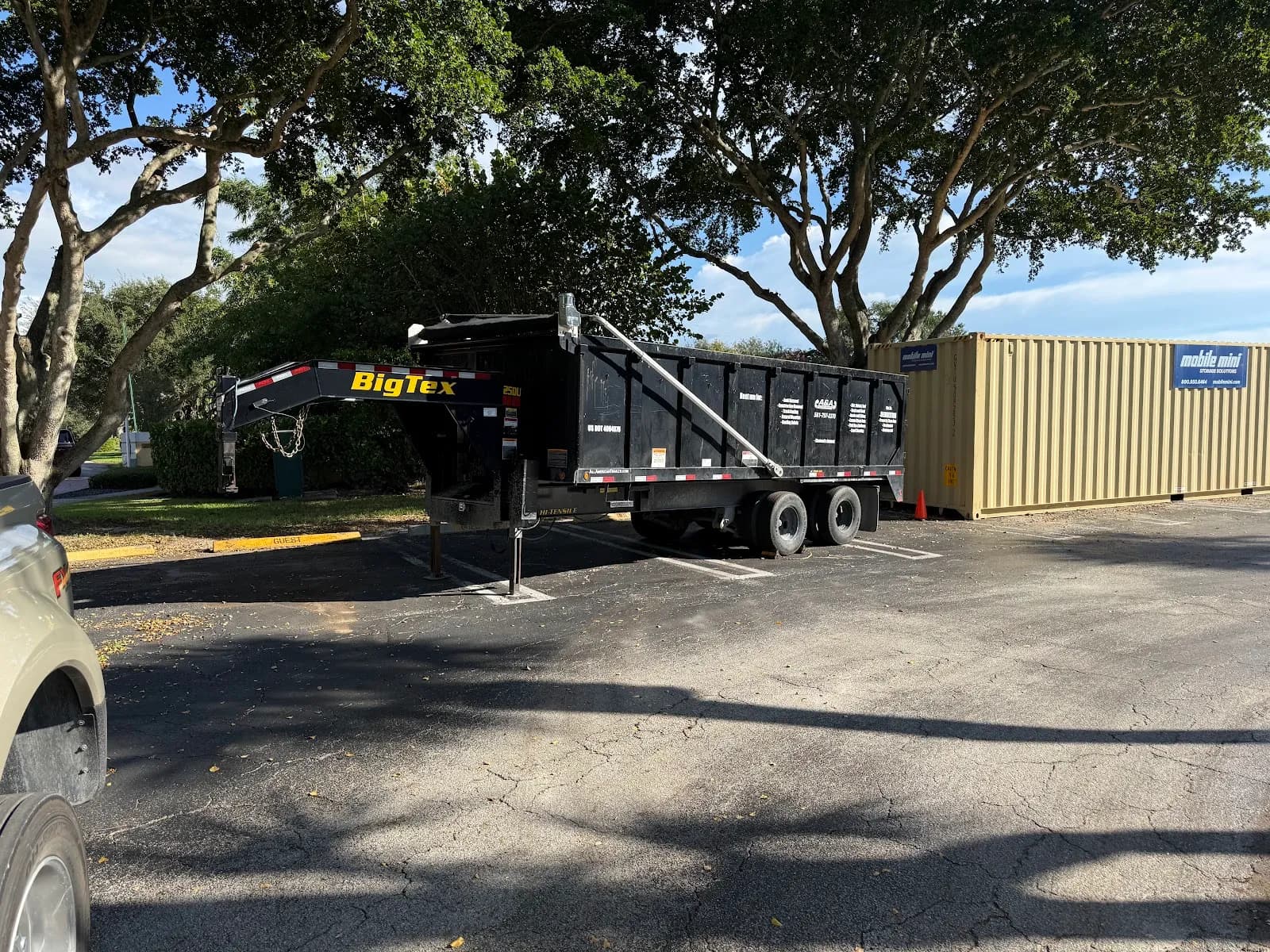 Black dump trailer parked next to a storage container in a lot